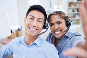 Smiling and diverse call center agents wearing headsets, sitting in a modern office environment, with a friendly and approachable demeanor.